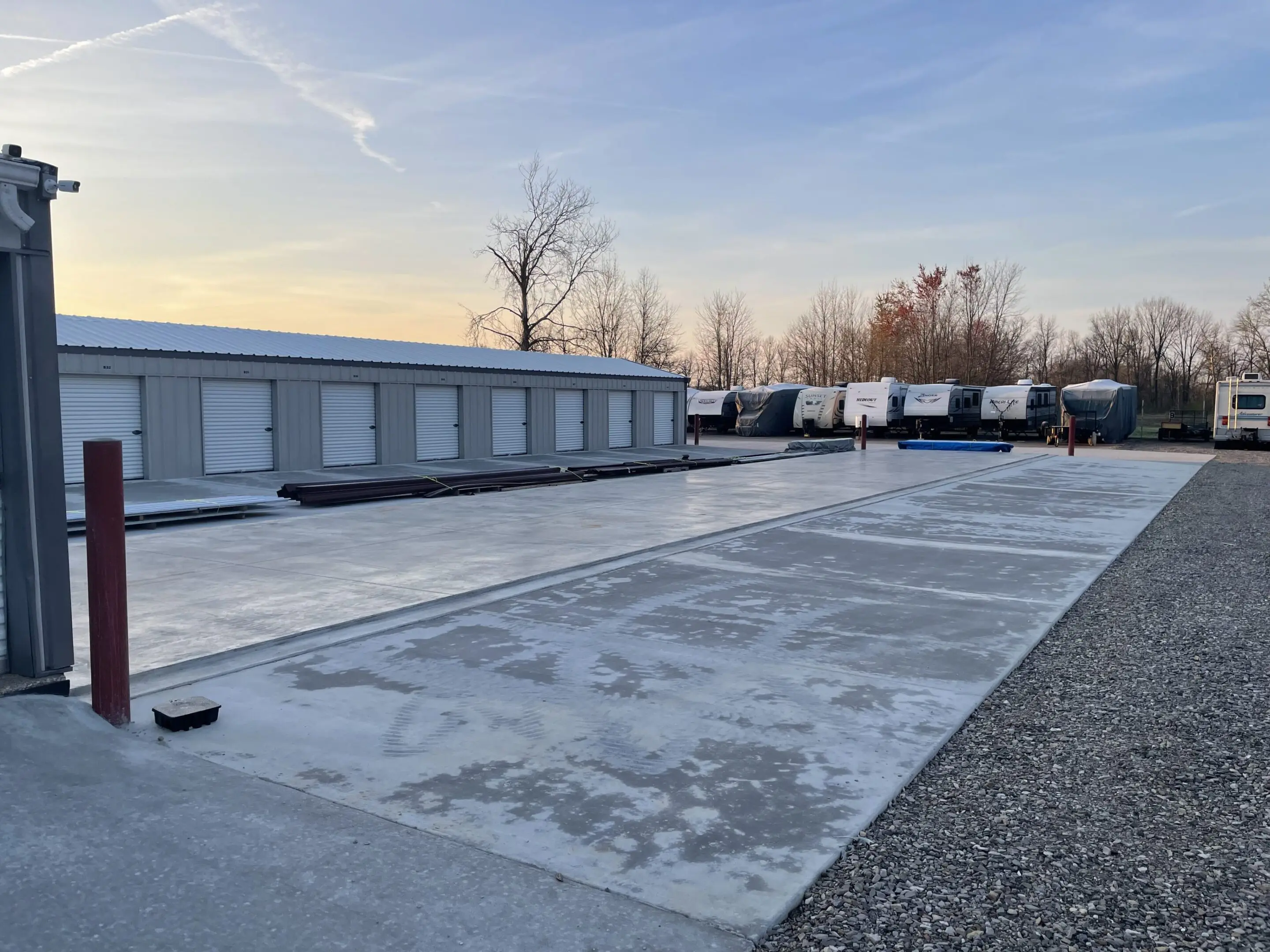 A parking area with multiple trucks and a storage building at sunset.